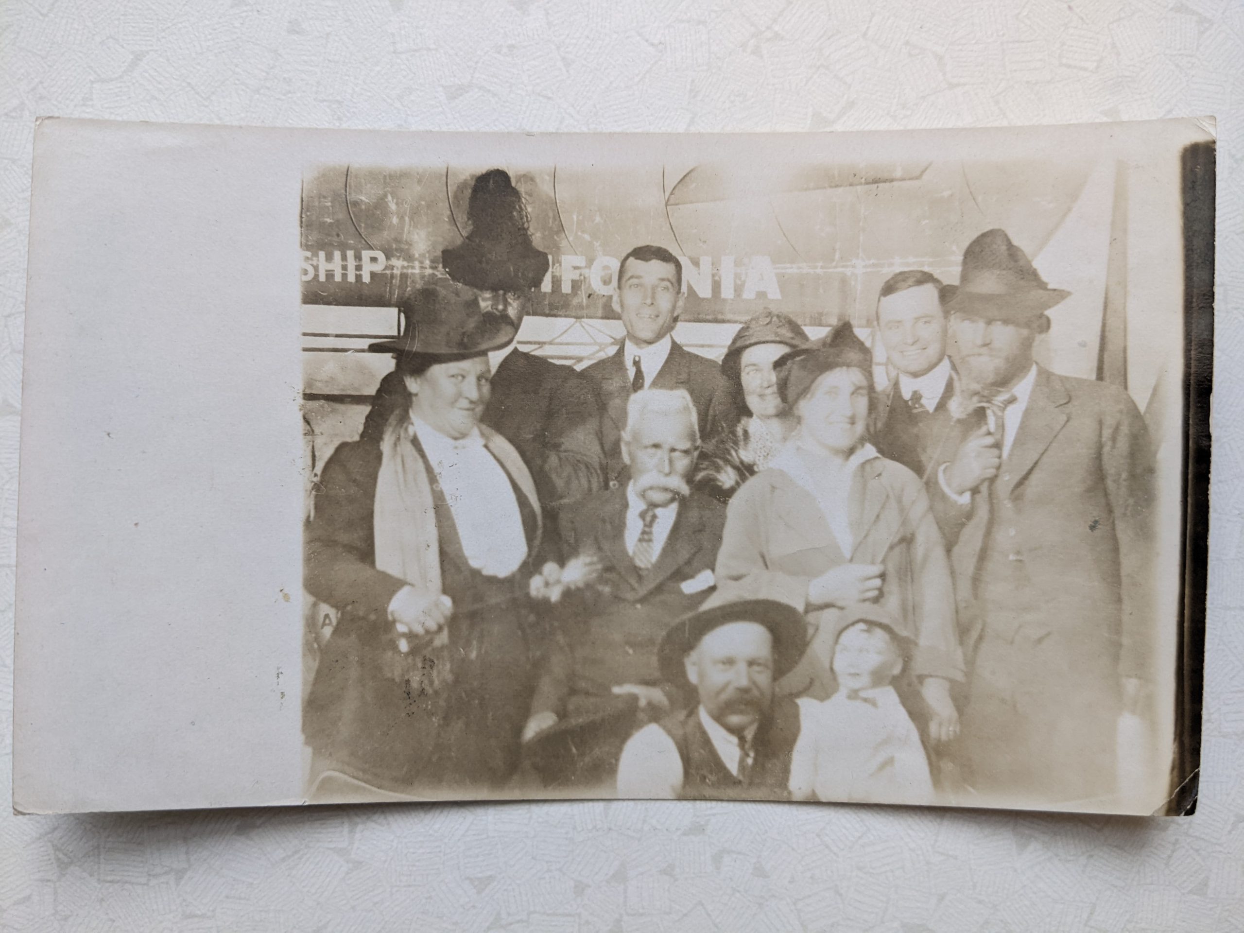 A faded photograph in sepia tones. Nine people and a doll or ventrioquist's dummy are grouped together and posing for the photograph. Some of them appear to be in fancy dress, but it's difficult to make out exactly what people are wearing.